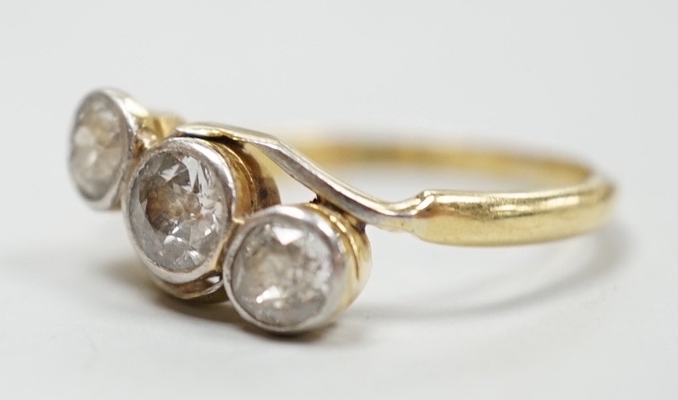 A yellow metal and three stone diamond set crossover ring, size N/O, gross weight 3.1 grams.